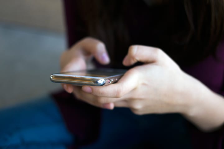 a photo of a woman's hands holding an iPhone 7, typing.