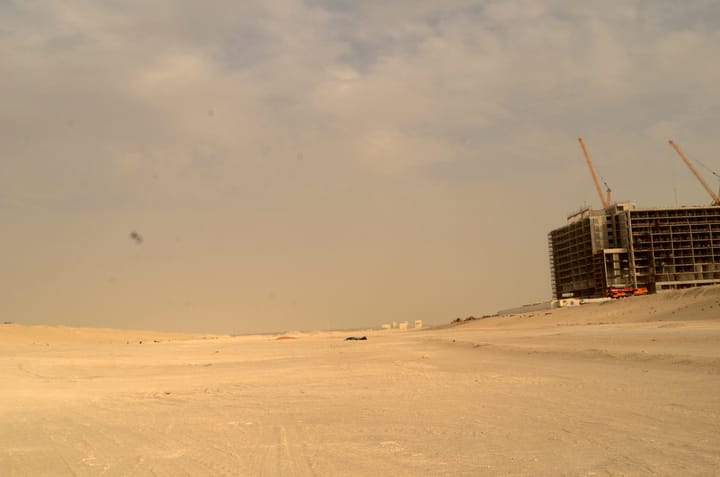 A photo of a desert with a construction site to the right. The sky is cloudy, and the entire pictures just feels very dusty.