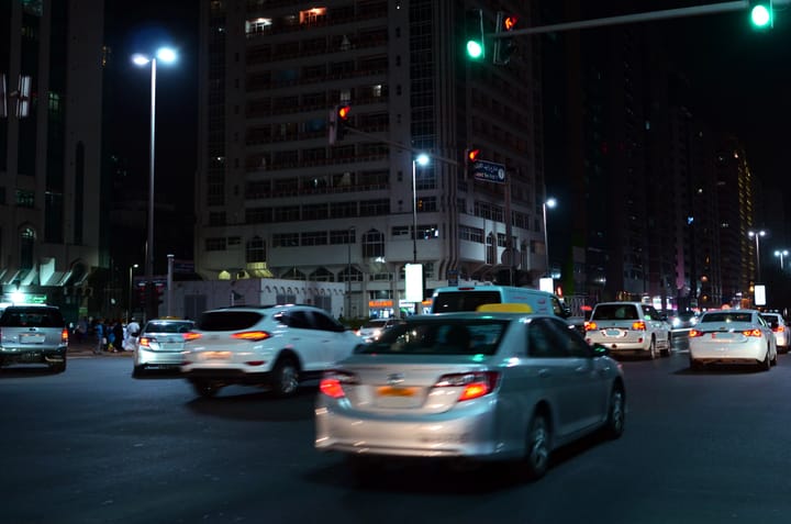 A photo of a nighttime road in Abu Dhabi, with cars whisking by. Their plate numbers are blurred in motion.