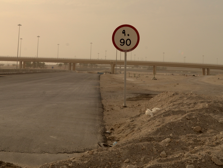 Desert road with a bridge in the distance. Empty road, a pile of dirt with some plastic sticking out. Road sign labeled "90".